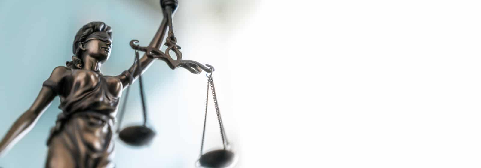 Nahaufnahme einer Justitia-Statue mit Schwert und Waage vor hellem Hintergrund