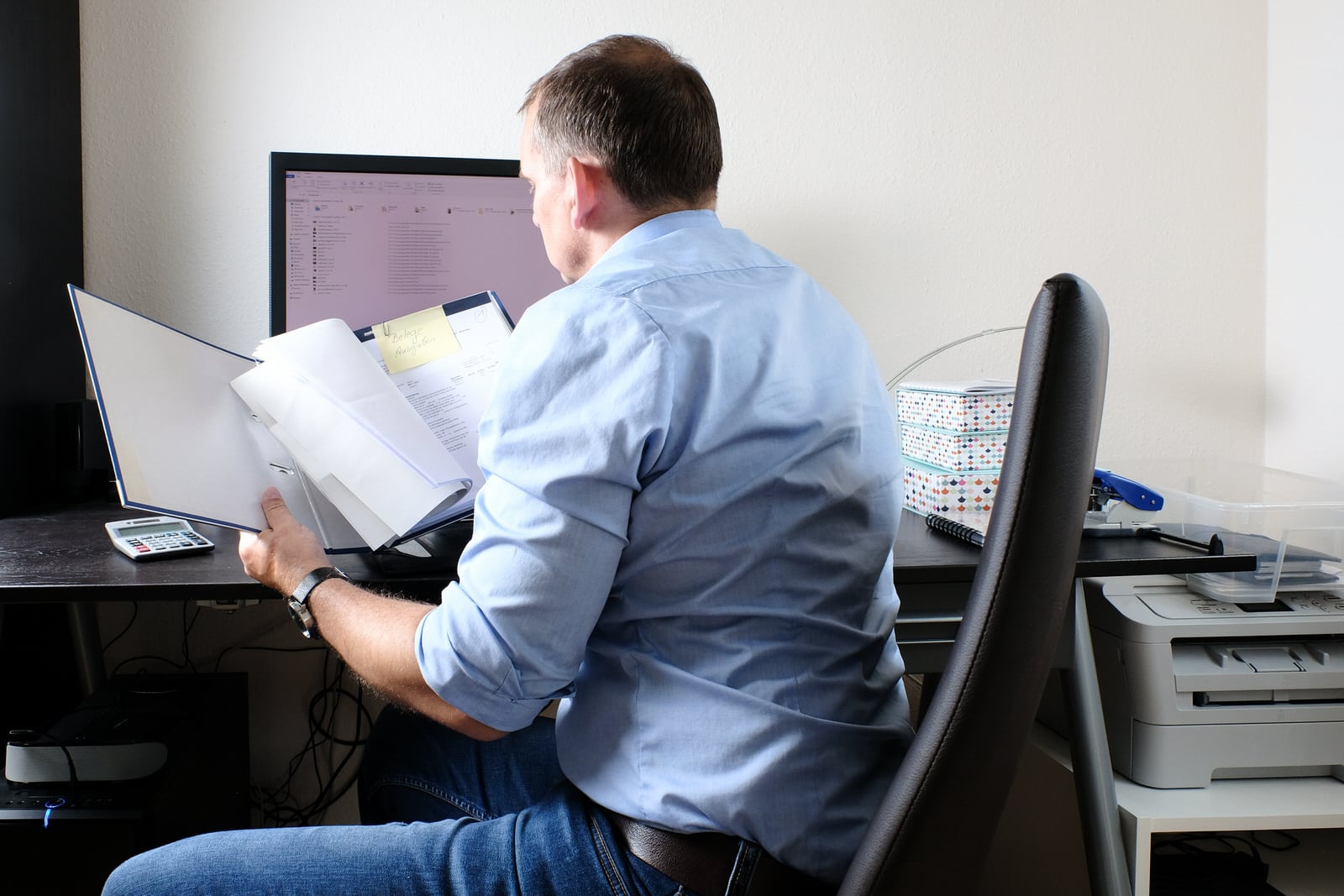 Sachbearbeiter sitzt am Schreibtisch vor einem Computer und bearbeitet Unterlagen.
