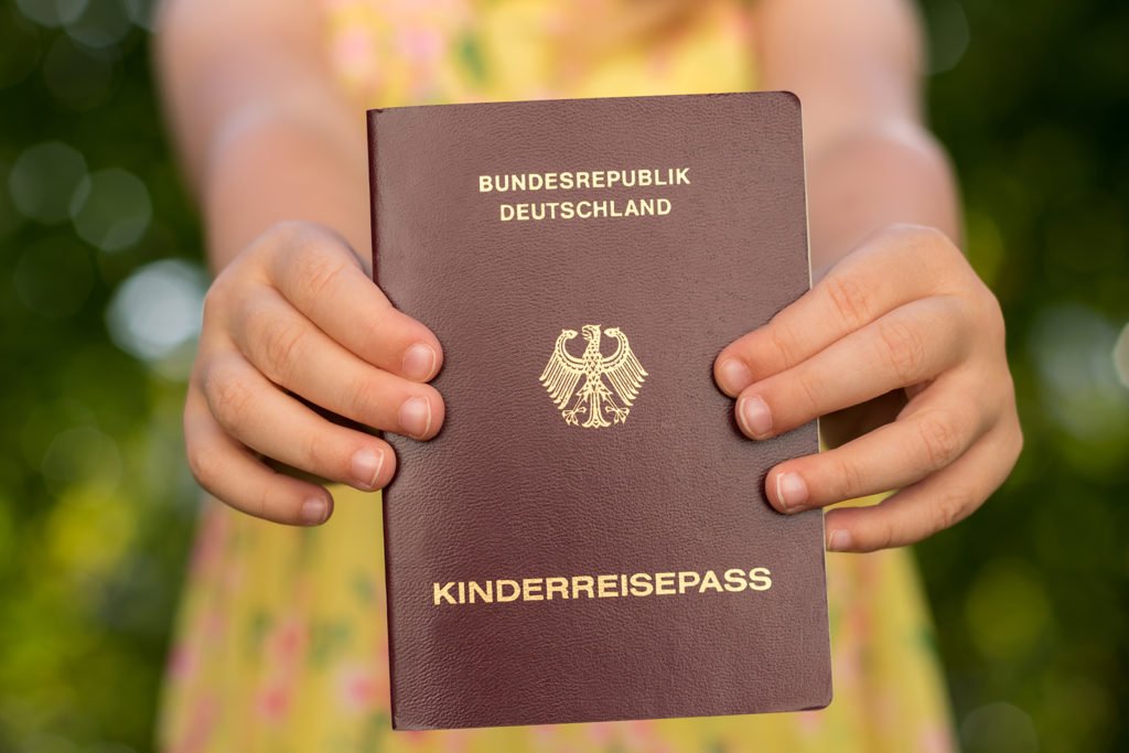 Ein Kind hält einen deutschen Kinderreisepass vor unscharfem grünem Hintergrund in den Händen.