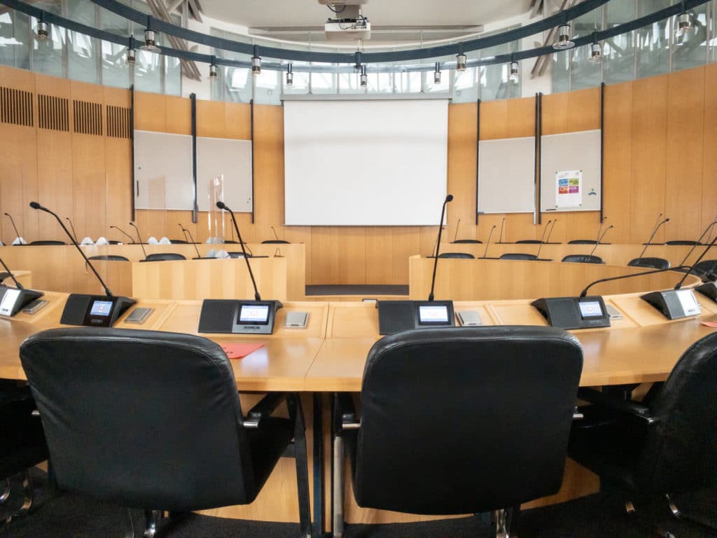 Ausschusssaal im Deggendorfer Rathaus Sitzungssaal mit runder Tischanordnung, Mikrofonen, Abstimmungsgeräten und großer Projektionsleinwand