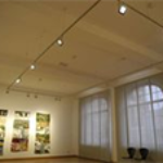Heller Innenraum eines kommunalen Gebäudes mit gerahmten Bildern an der Wand, großen Fenstern und Sitzgelegenheiten.