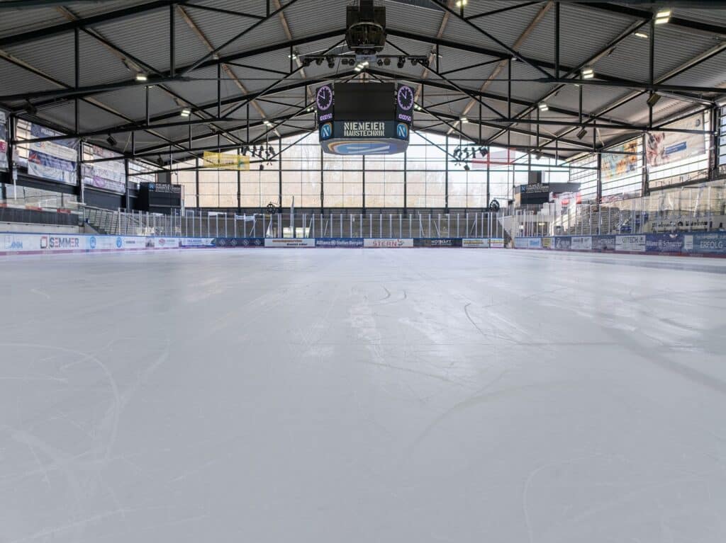 Blick über die Eisfläche des Eisstadions mit Tribünen, Werbebanden und Anzeigetafel