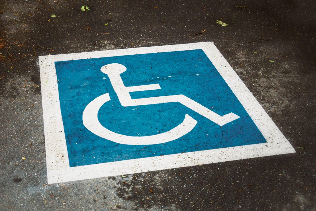 Blau-weißes Rollstuhl-Piktogramm für einen barrierefreien Parkplatz auf dem Asphalt.