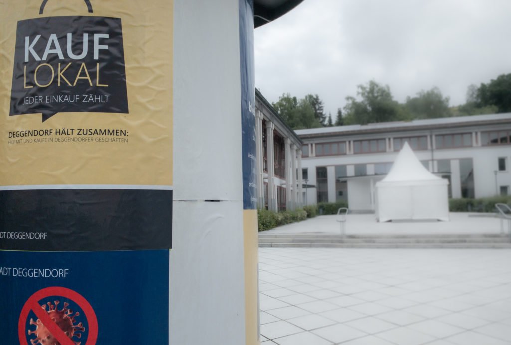 Plakat mit der Aufschrift „Kauf lokal – jeder Einkauf zählt“ neben einem leeren Rathausplatz in Deggendorf