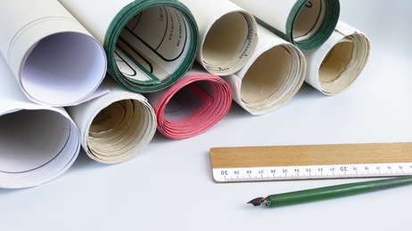 Mehrere gerollte Papierbahnen in verschiedenen Farben liegen neben einem Lineal und einem grünen Zeichenstift.